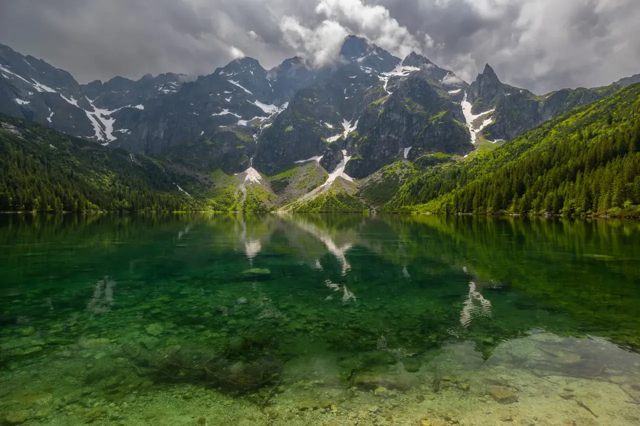 Morskie Oko z rowerem w tle, odbijające się w krystalicznie czystej wodzie. Majestatyczne góry i gęsty las tworzą malowniczy krajobraz.