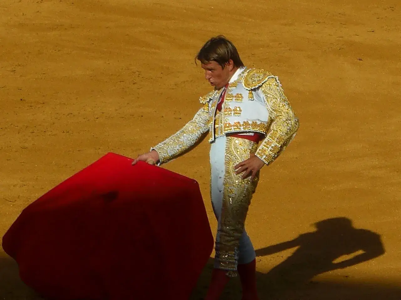 Torero con traje de luces, listo para la faena de muleta, con la capa roja extendida en la arena.