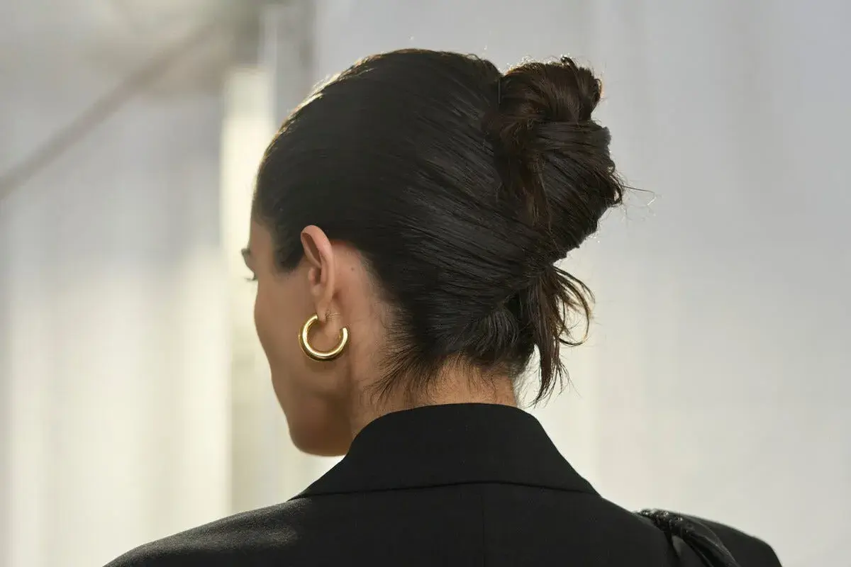 Capelli raccolti in uno chignon elegante, con un look effetto bagnato che dona lucentezza. Orecchino a cerchio dorato.