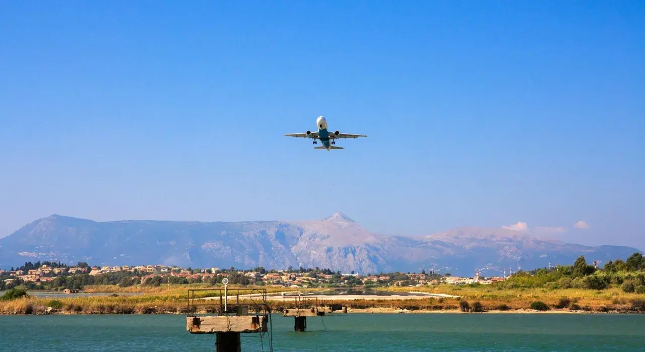 Airplane ascending over a coastal town near the Sicily airport, with mountains in the background.