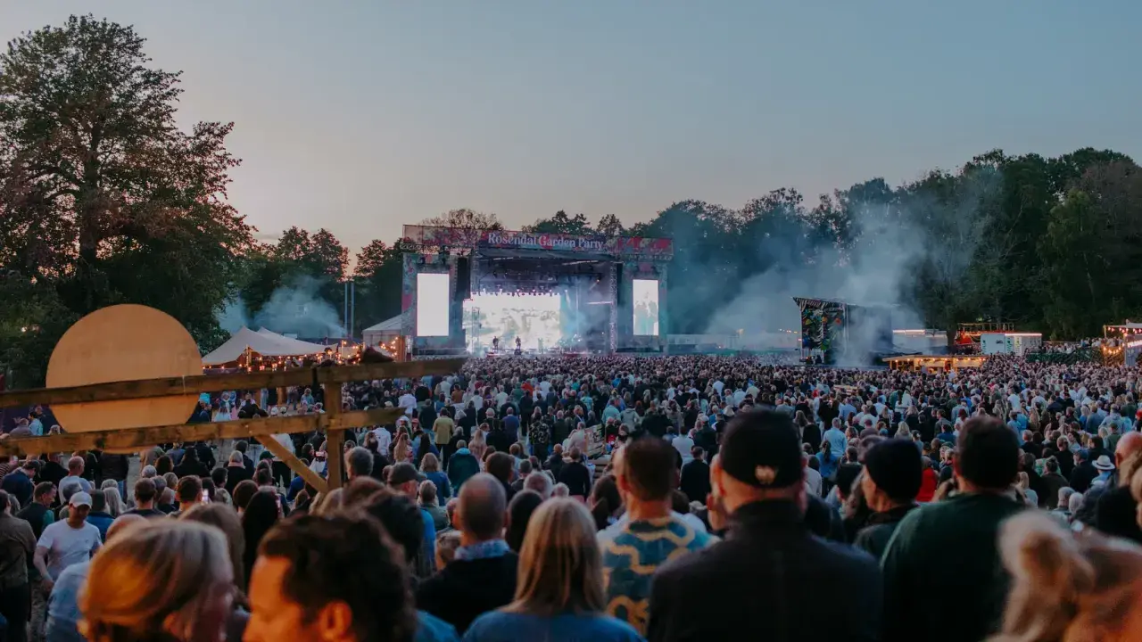Stor publik vid Rosendal Garden Party. En stor scen med artister och ljusspel, omgiven av träd och tält.