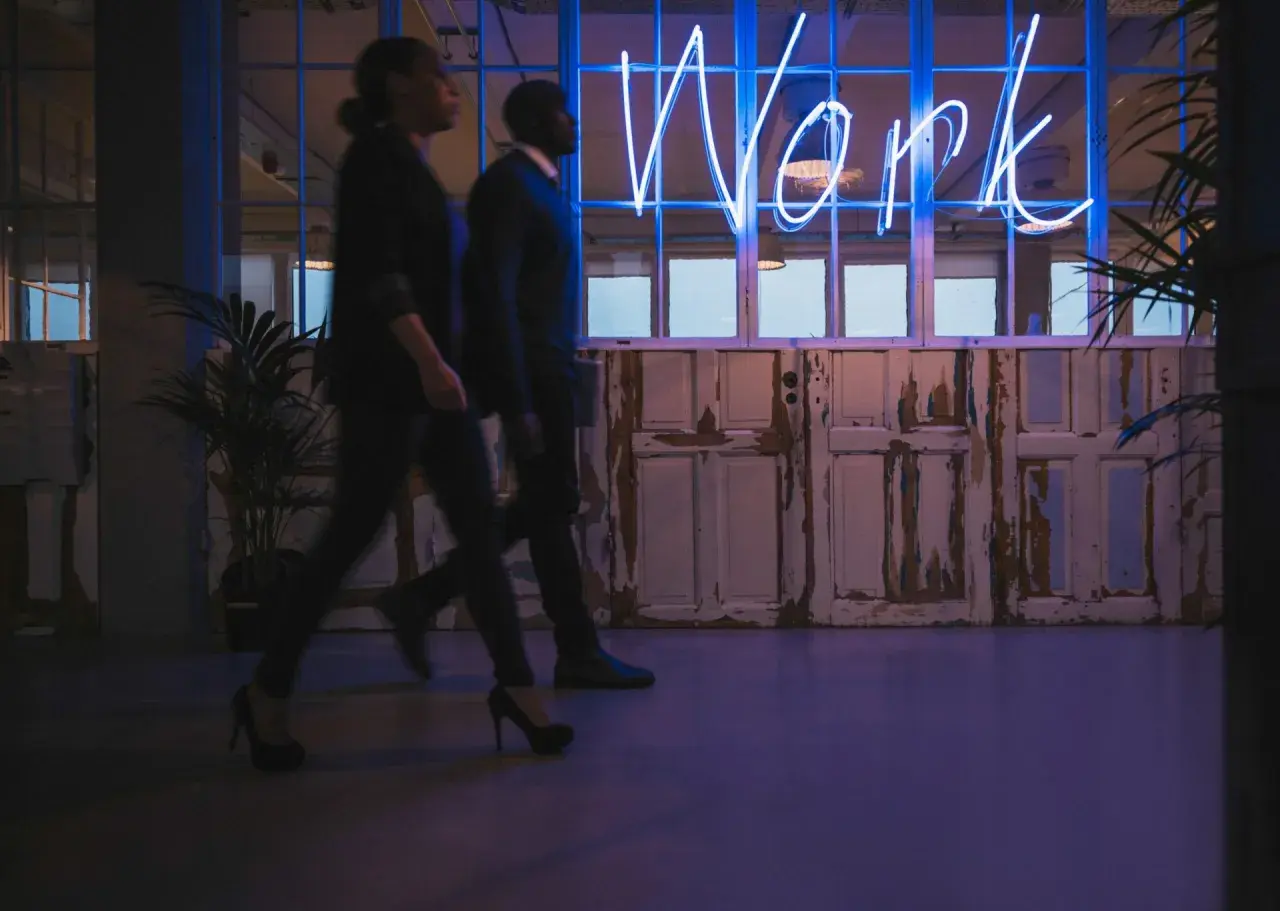 Ludzie idą w stronę neonu "Work", symbolizującego misję i wizję firmy.