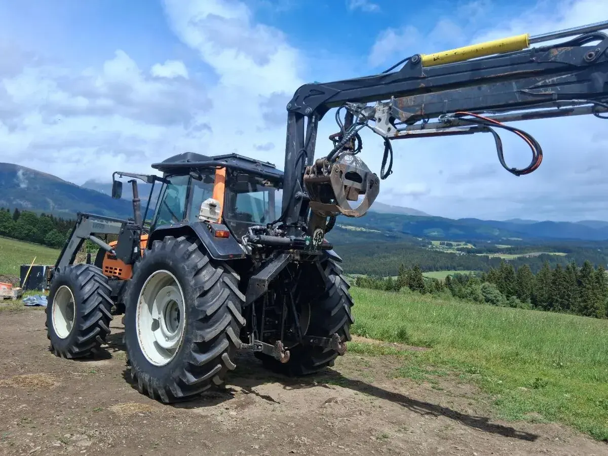Ein gebrauchter Forstkran mit Greifer an einem Traktor, bereit für den Einsatz im Wald.