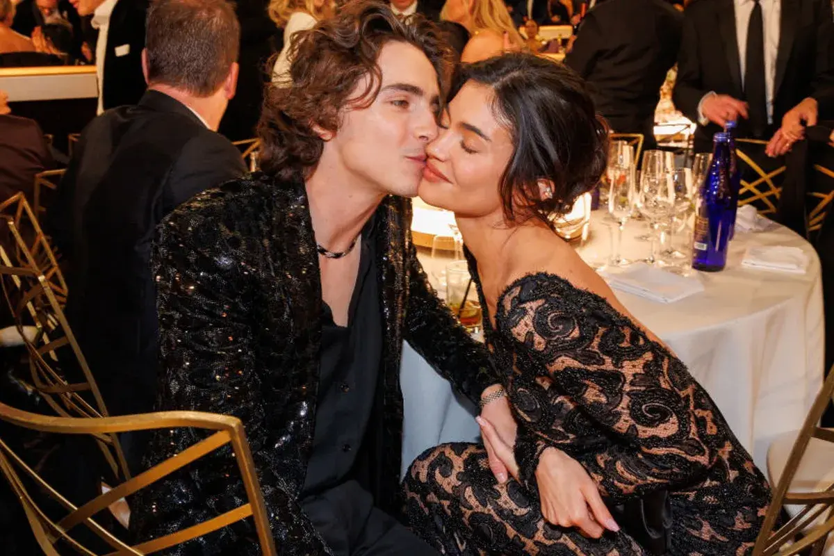 Kylie Jenner i Timothée Chalamet w czarnych, eleganckich strojach, podczas romantycznego momentu przy stole.