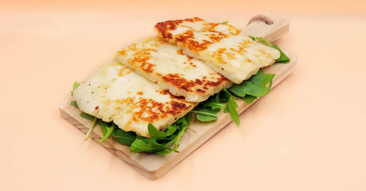 Usmażony ser halloumi na desce z rukolą.