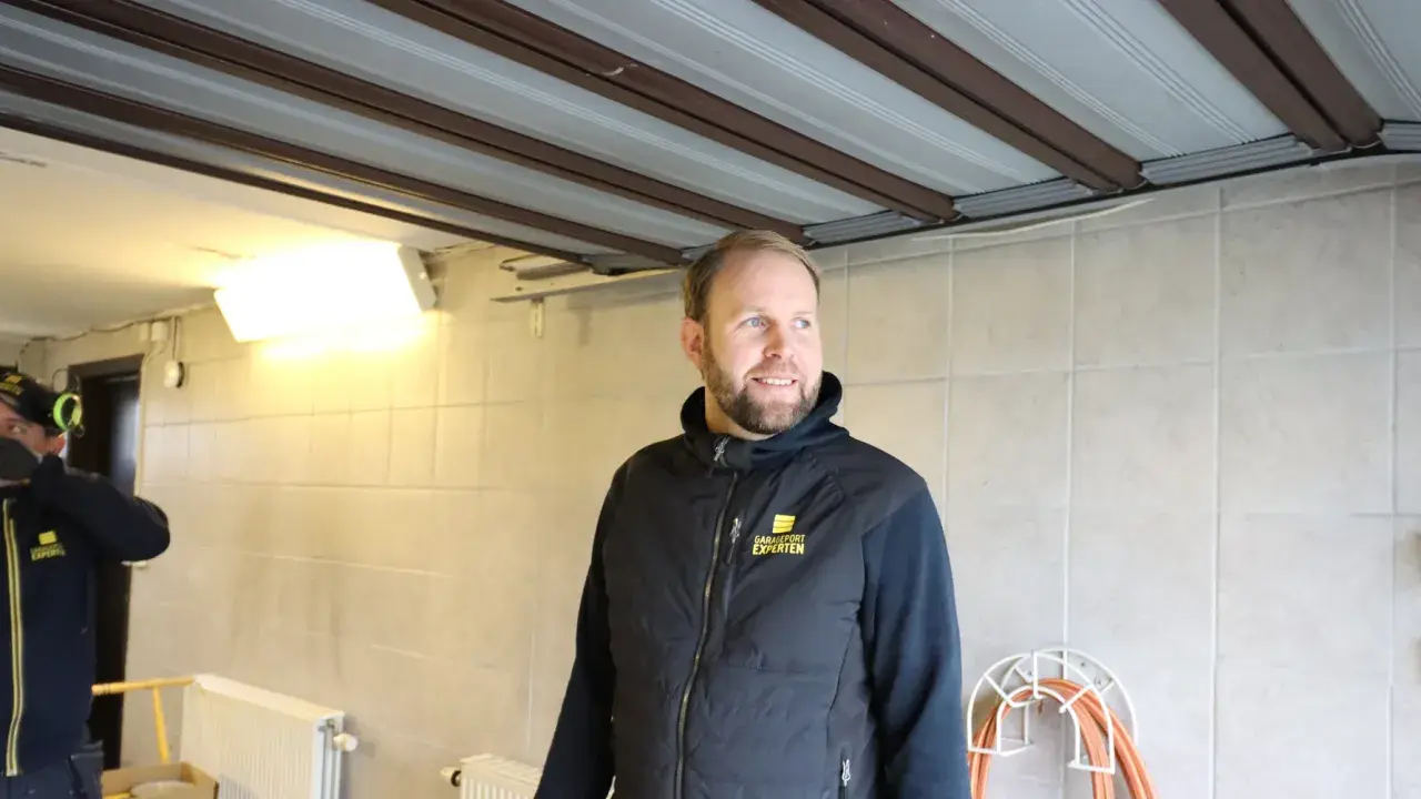 Man i väst med texten "Garageportexperten" ler. Ovanför syns en **täta garageport** i taket.