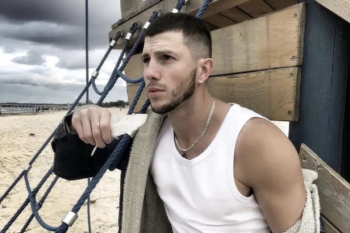 Sasha top model, z piórkiem w dłoni, na tle plaży i chmur.