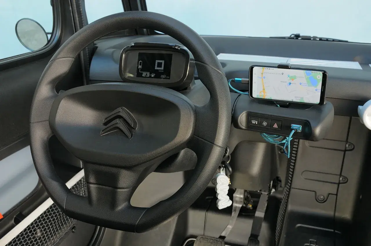 Interno Citroen Ami: volante, cruscotto digitale con indicatore di velocità e autonomia, smartphone con navigatore. La velocità massima è un dettaglio da scoprire!