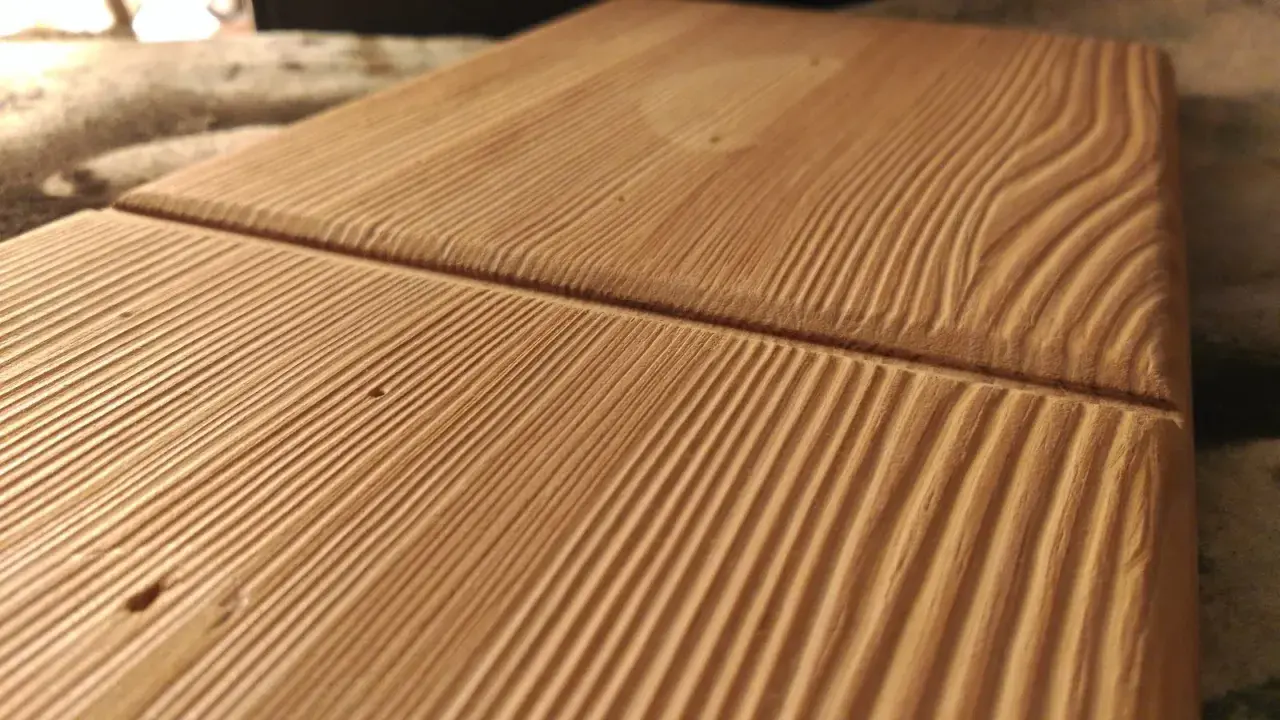 Superficie de madera con surcos paralelos que resaltan las vetas naturales. La luz crea sombras que dan profundidad a la textura.