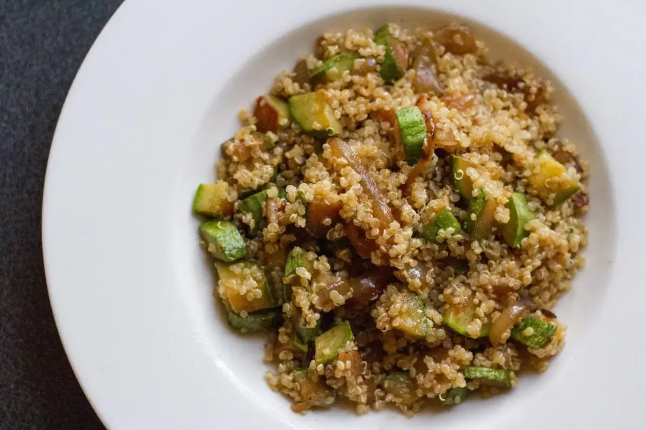 Un piatto di quinoa con verdure, tra cui zucchine a cubetti e cipolle caramellate, servito su un piatto bianco.