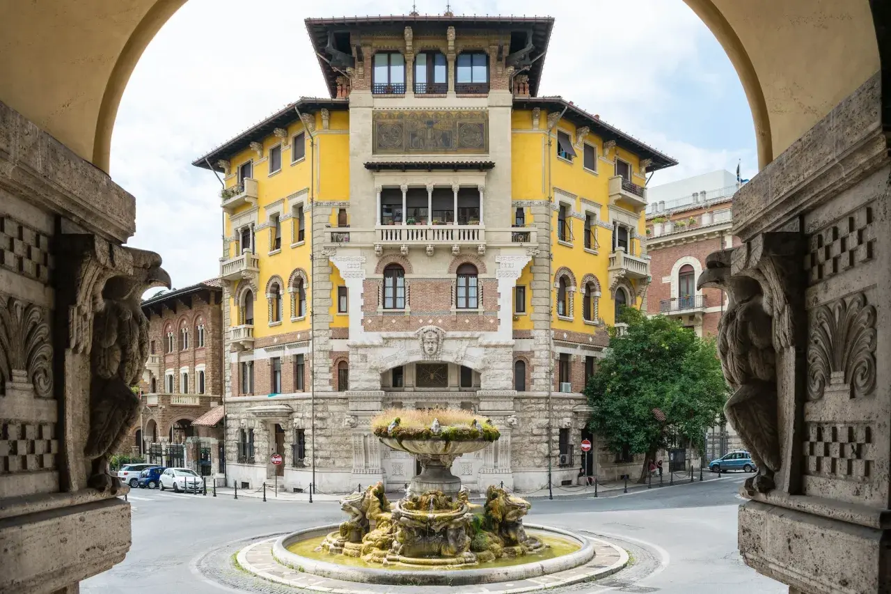 Fontana e palazzo giallo in stile Coppedè, con dettagli scultorei e un'atmosfera d'altri tempi.
