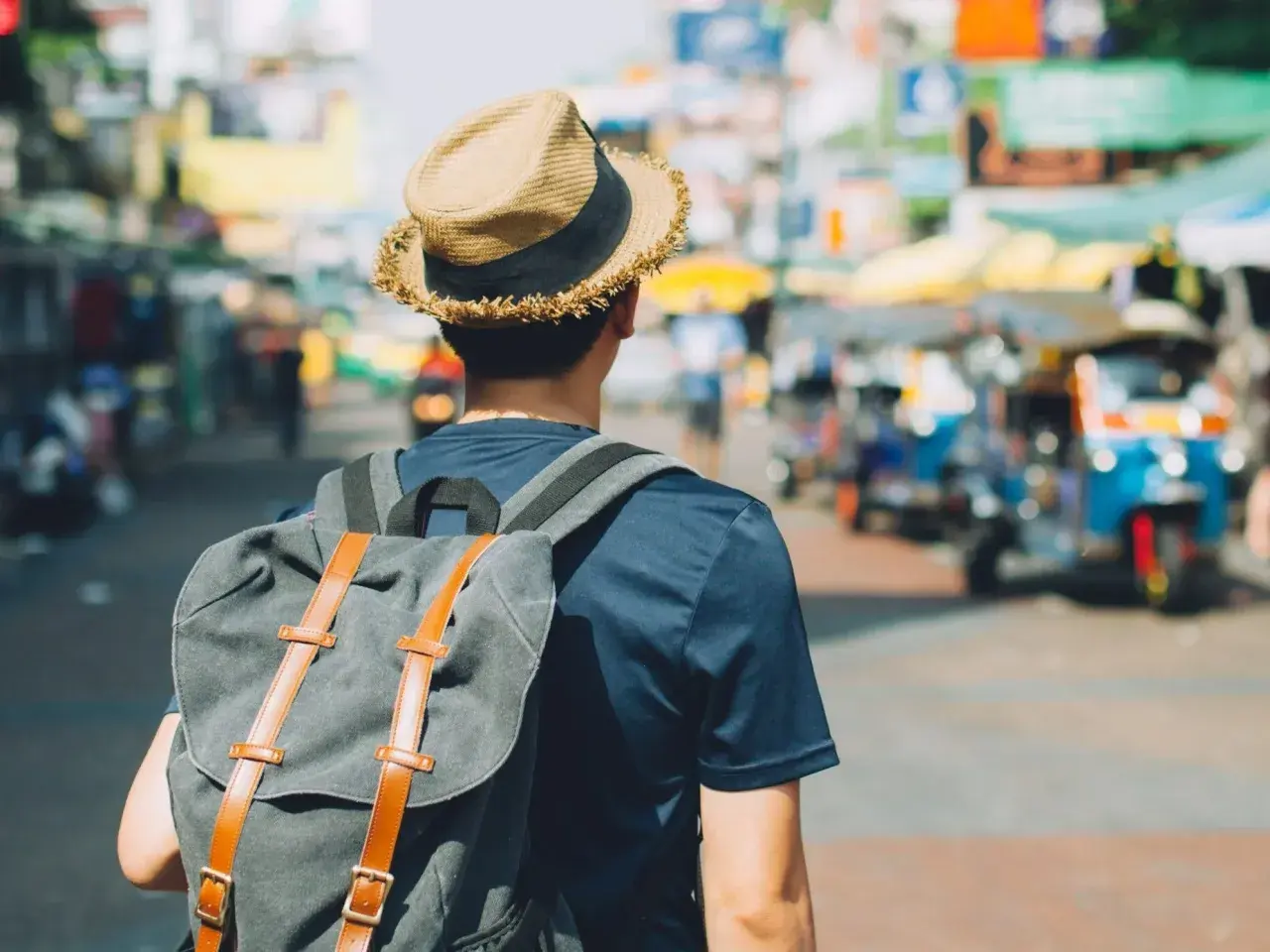 Mężczyzna w kapeluszu i z plecakiem na tle tętniącego życiem azjatyckiego miasta. Poznaj jego travel hacks!