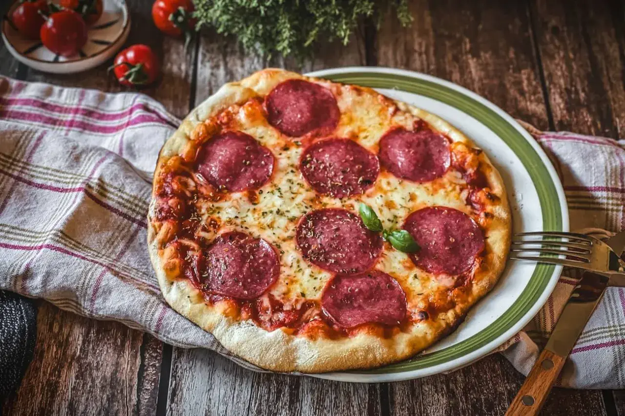 Eine köstliche Pizza Salami mit geschmolzenem Käse und frischem Basilikum auf einem Holztisch.