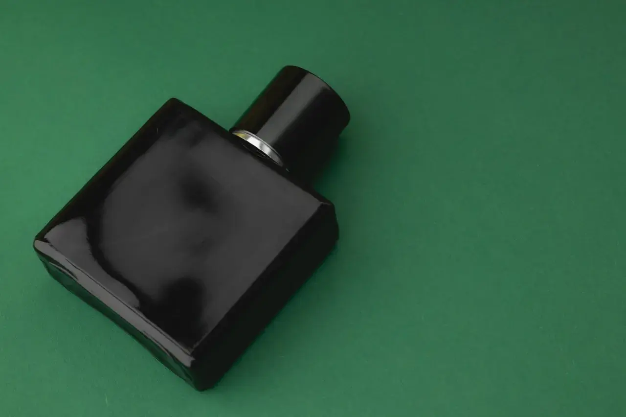 Czarna butelka perfum z nutami **vetiver** na zielonym tle.