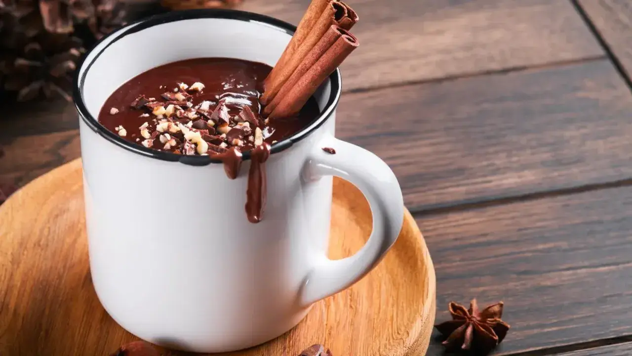 Un déliceux chocolat chaud crémeux, garni de noisettes concassées et de bâtons de cannelle, prêt à réchauffer vos journées.