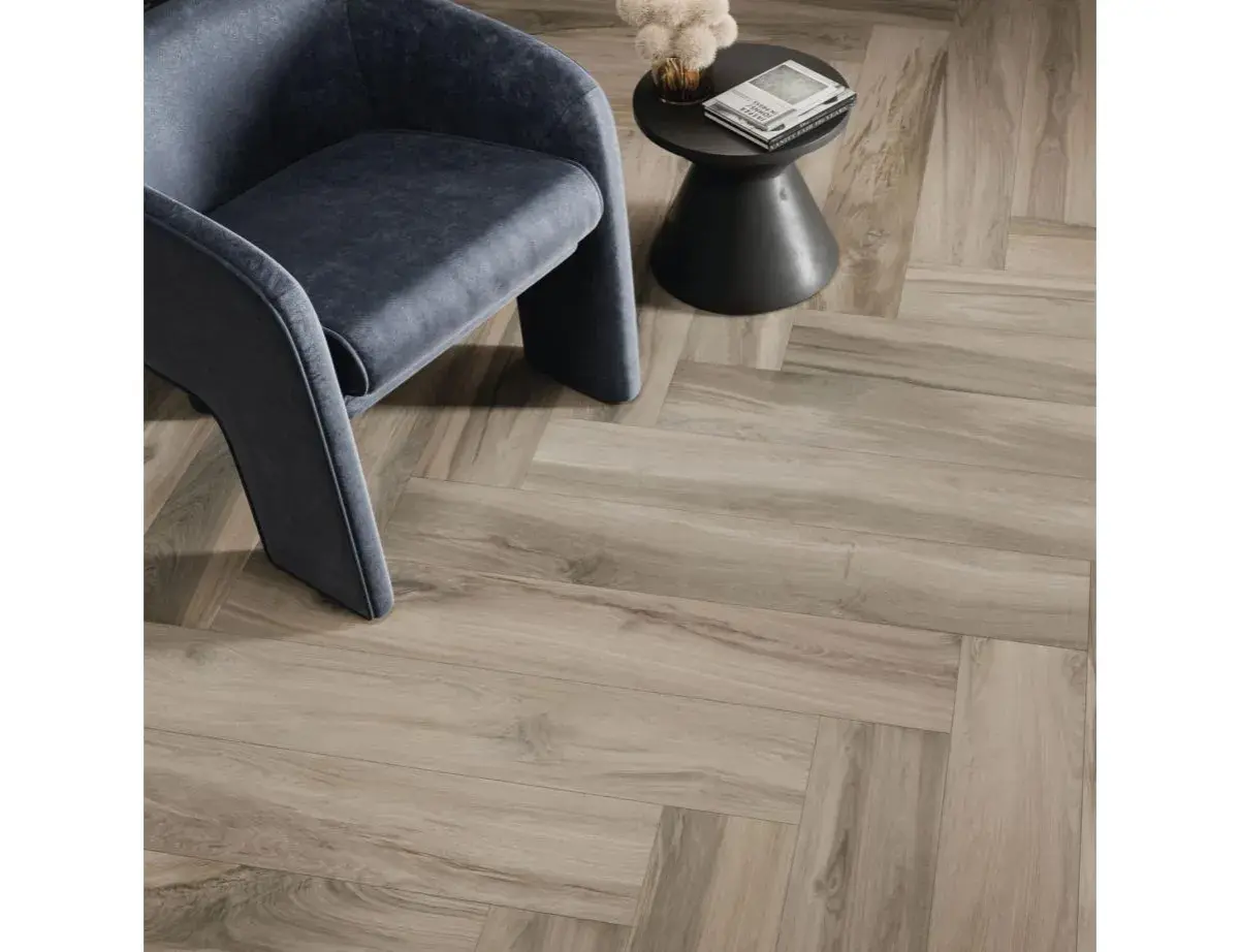 Un fauteuil moderne repose sur un sol en pose carrelage imitation parquet en chevrons, créant une ambiance chaleureuse et élégante.
