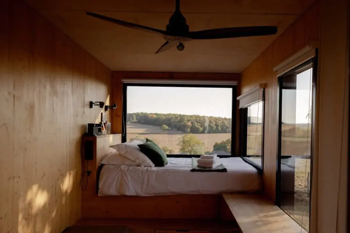 Intérieur d'une tiny house avec un lit douillet et une vue panoramique sur la campagne. Un endroit parfait pour se ressourcer.