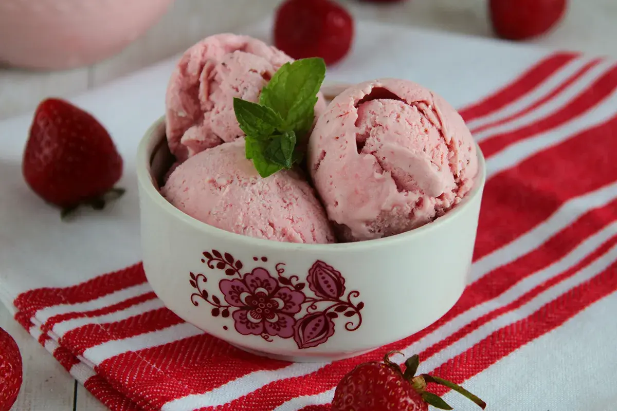 Pyszne lody truskawkowe w miseczce, ozdobione miętą. Idealne na lato, pokazują, jak zrobić lody truskawkowe.