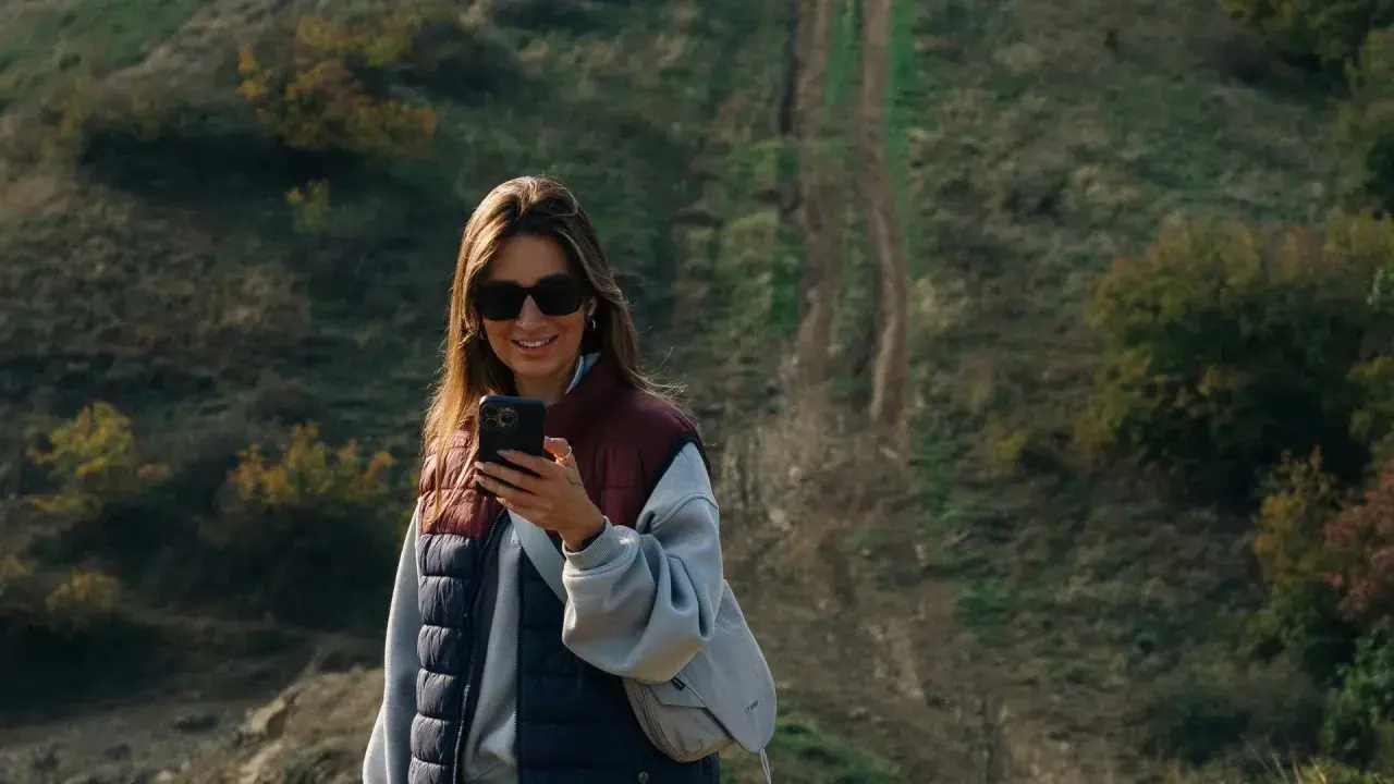 Kobieta z telefonem na tle pagórkowatego krajobrazu, idealnego do **roaming Wielka Brytania**.