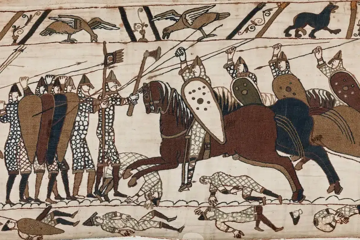 Scen från slaget vid Hastings 1066. Soldater med sköldar och spjut, en ryttare på häst. Nedanför fallna krigare.