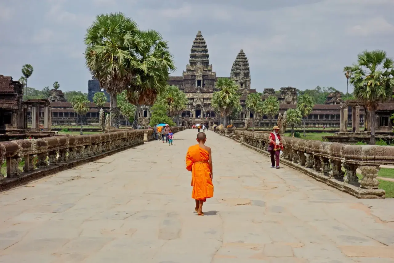 Mnich w pomarańczowej szacie idzie w stronę Angkor Wat, symbolu kambodżańskiej wycieczki.