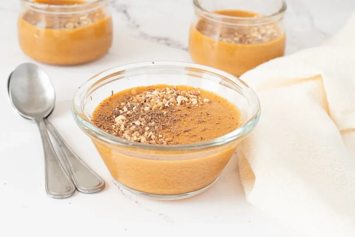 Delicioso postre cremoso, como baba de camelo, servido en un cuenco de cristal y espolvoreado con frutos secos y virutas de chocolate.