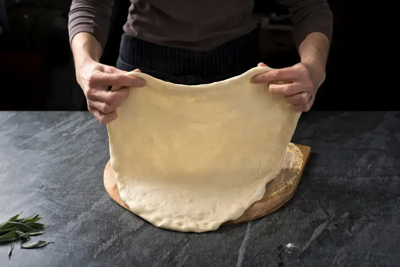 Ręce rozciągają elastyczne ciasto na pizzę, idealne do szybkiego przepisu na ciasto do pizzy.