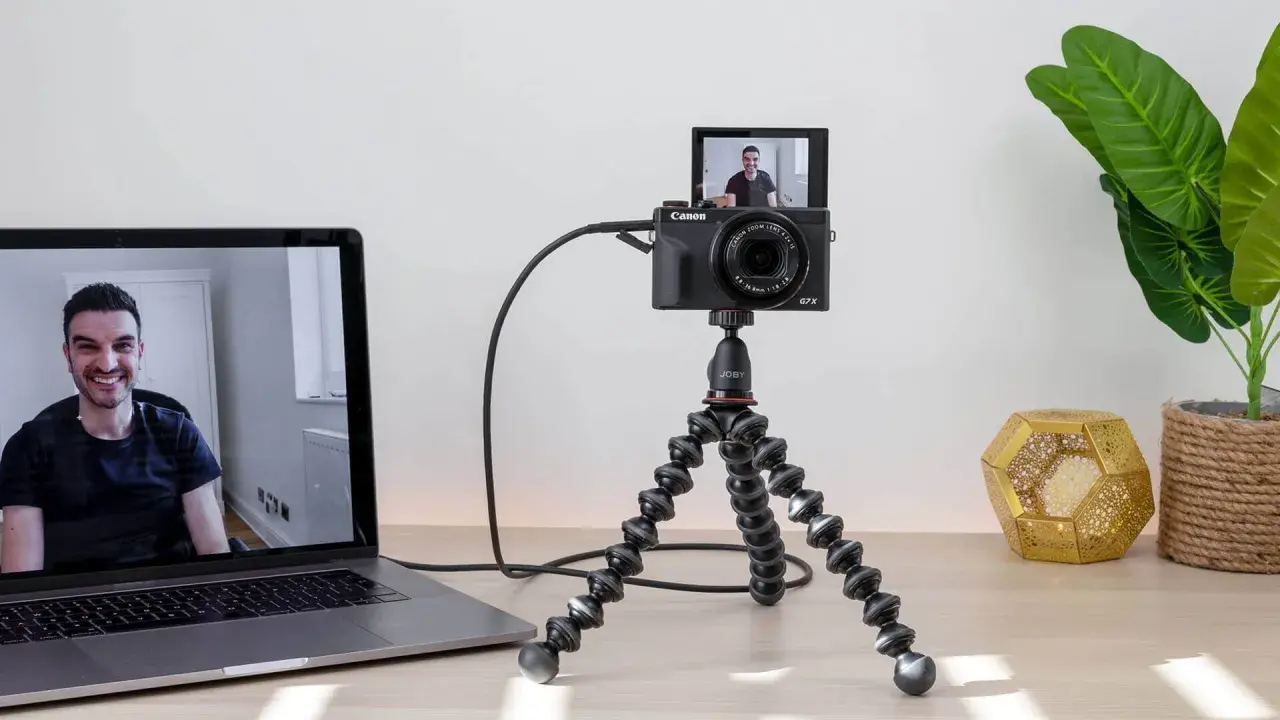 Configuración para usar webcam como cámara de seguridad: una Canon G7X en un trípode flexible, conectada a un portátil que muestra a un hombre sonriendo.