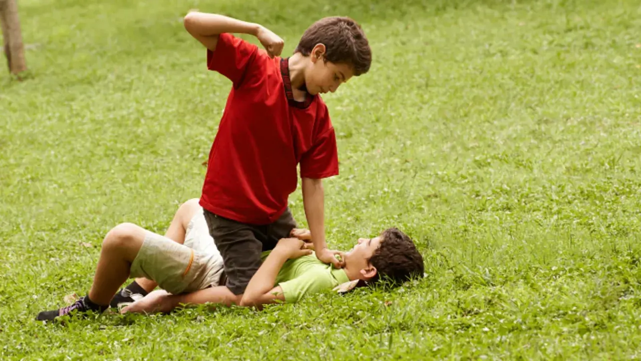 Un niño en camiseta roja agrede a otro en el suelo. Un ejemplo de cómo los niños que excluyen a otros pueden causar daño.