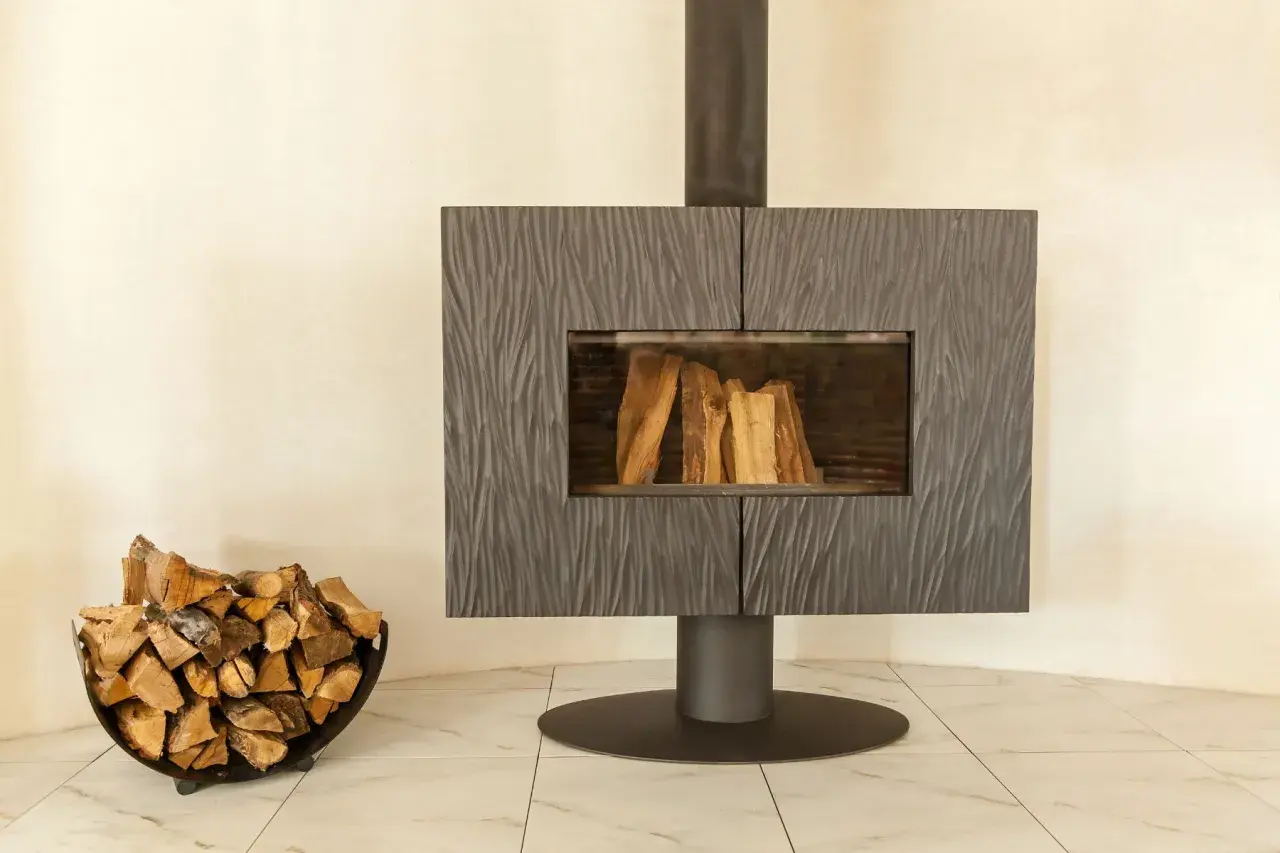 Un poêle moderne avec une cheminée vitrée et du bois de chauffage dans un panier. La **déco derrière un poêle** est sobre, mettant en valeur l'âtre.