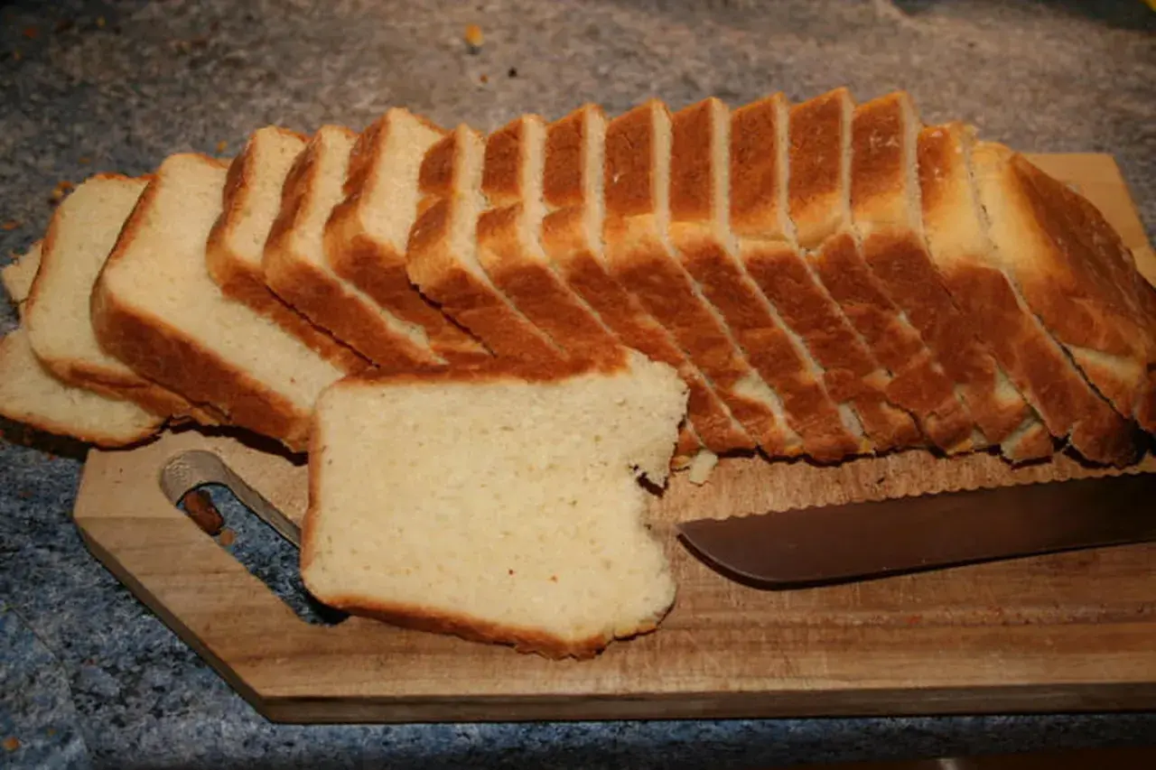 Tranches de pâte à pain de mie dorées et moelleuses, prêtes à être dégustées sur une planche en bois avec un couteau.