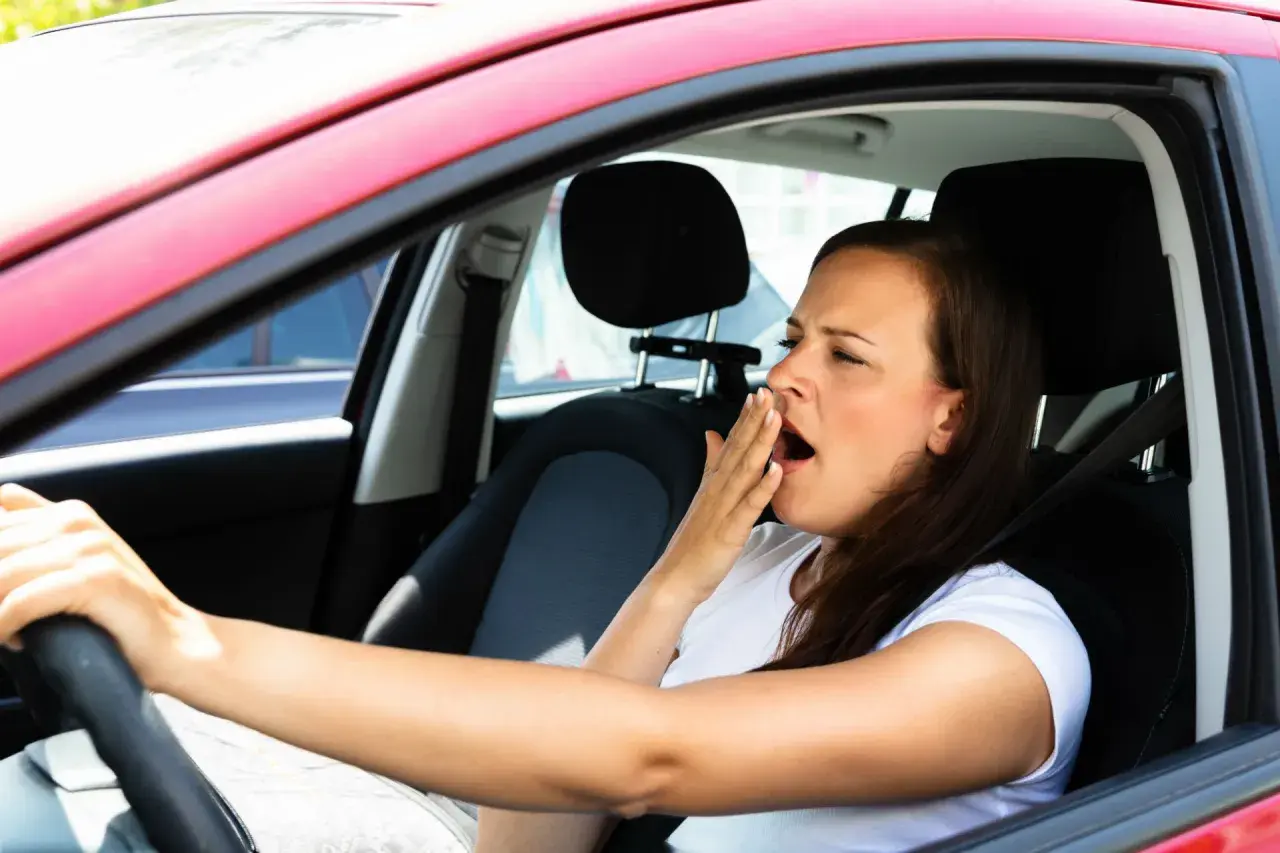 Mujer bosteza al volante, un claro ejemplo de qué puede causar somnolencia en un conductor.