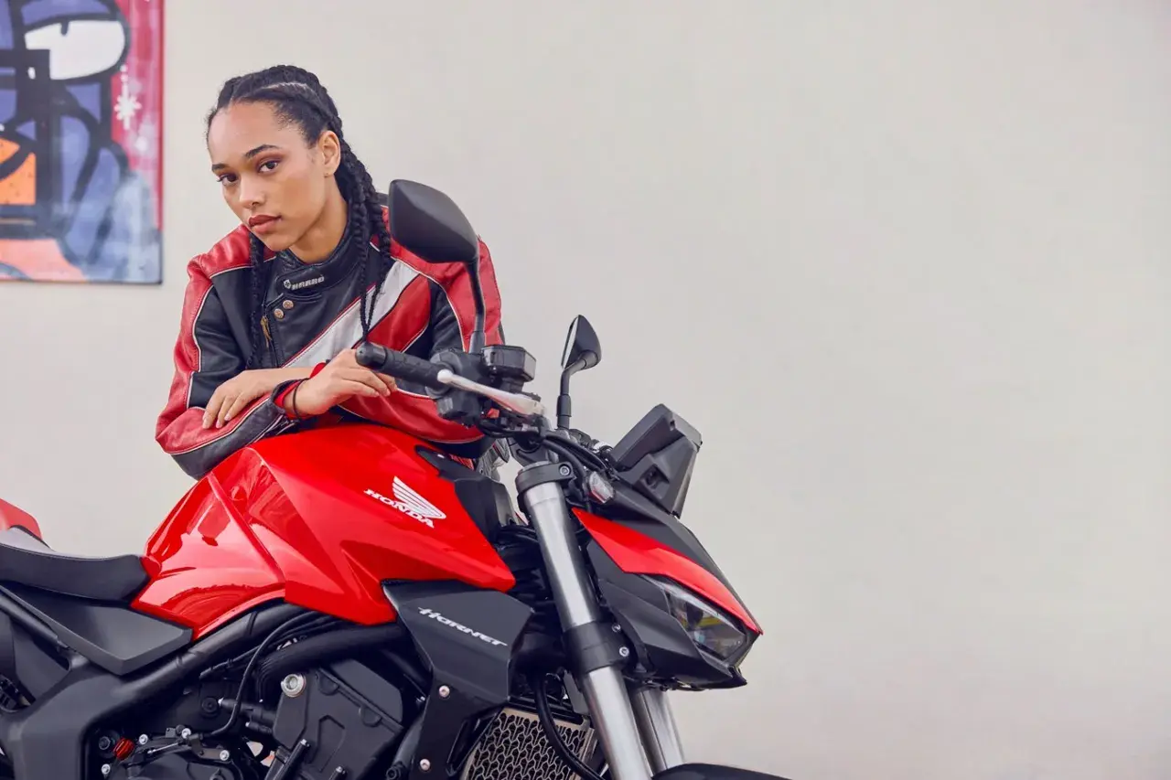 Joven con chaqueta de cuero posa junto a una moto roja Honda Hornet. Lista para el rodaje moto 125.