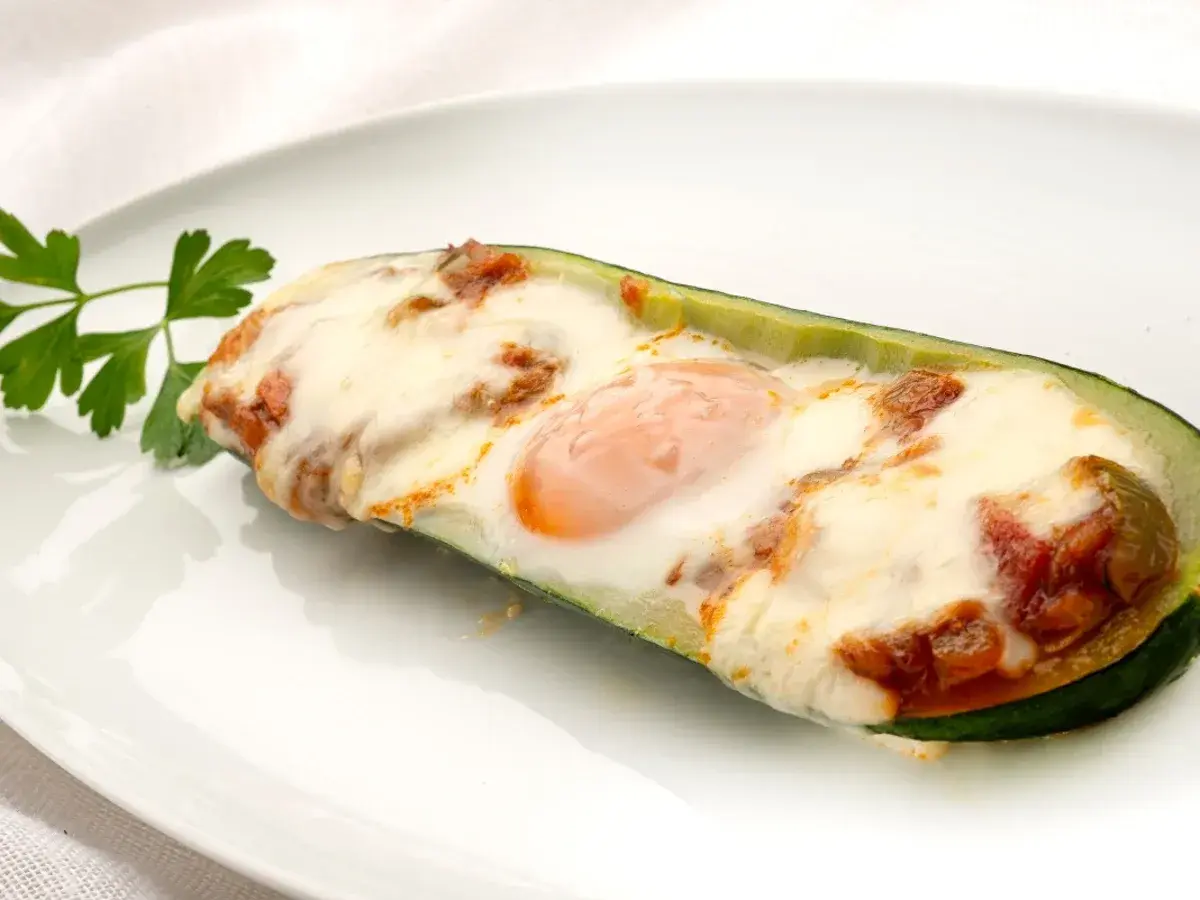 Deliciosos calabacines rellenos con huevo y queso gratinado, adornados con perejil fresco.
