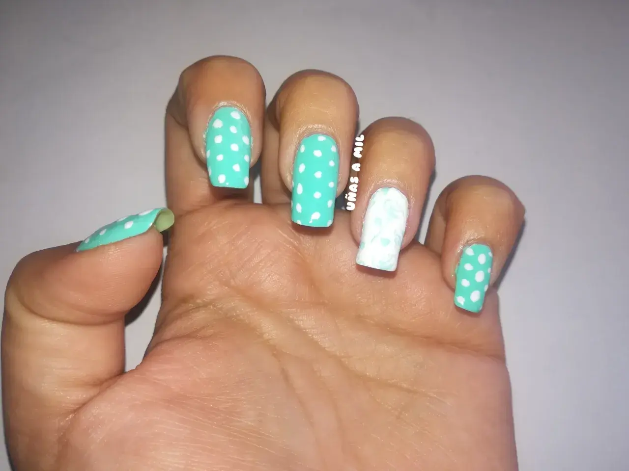 Uñas sevillanas con diseño de lunares turquesa y blanco, y un dedo decorado con un delicado estampado floral.