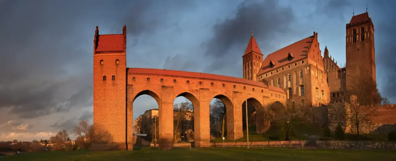 Imponujące zamki na Pomorzu, z cegły i czerwonym dachem, oświetlone zachodzącym słońcem, na tle burzowego nieba.
