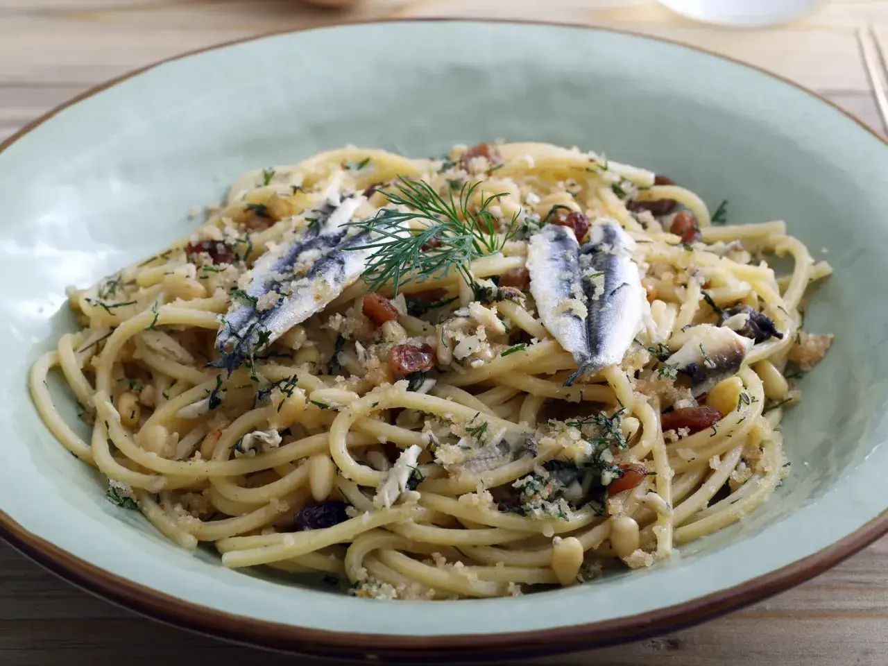 Un plat de pâtes aux sardines, garni de pignons de pin, de raisins secs et d'aneth frais.