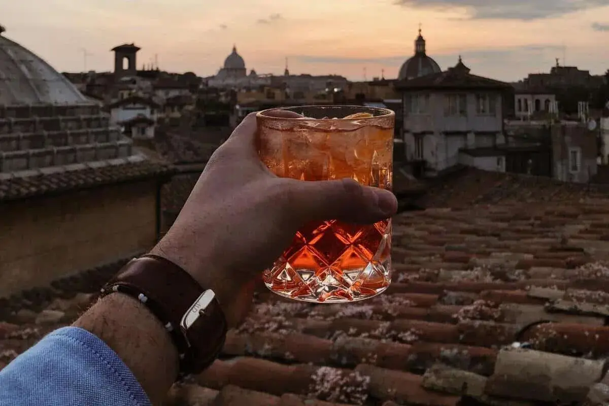 Un bicchiere di aperitivo con vista sui tetti di Roma centro al tramonto. Un momento perfetto per un apericena indimenticabile.