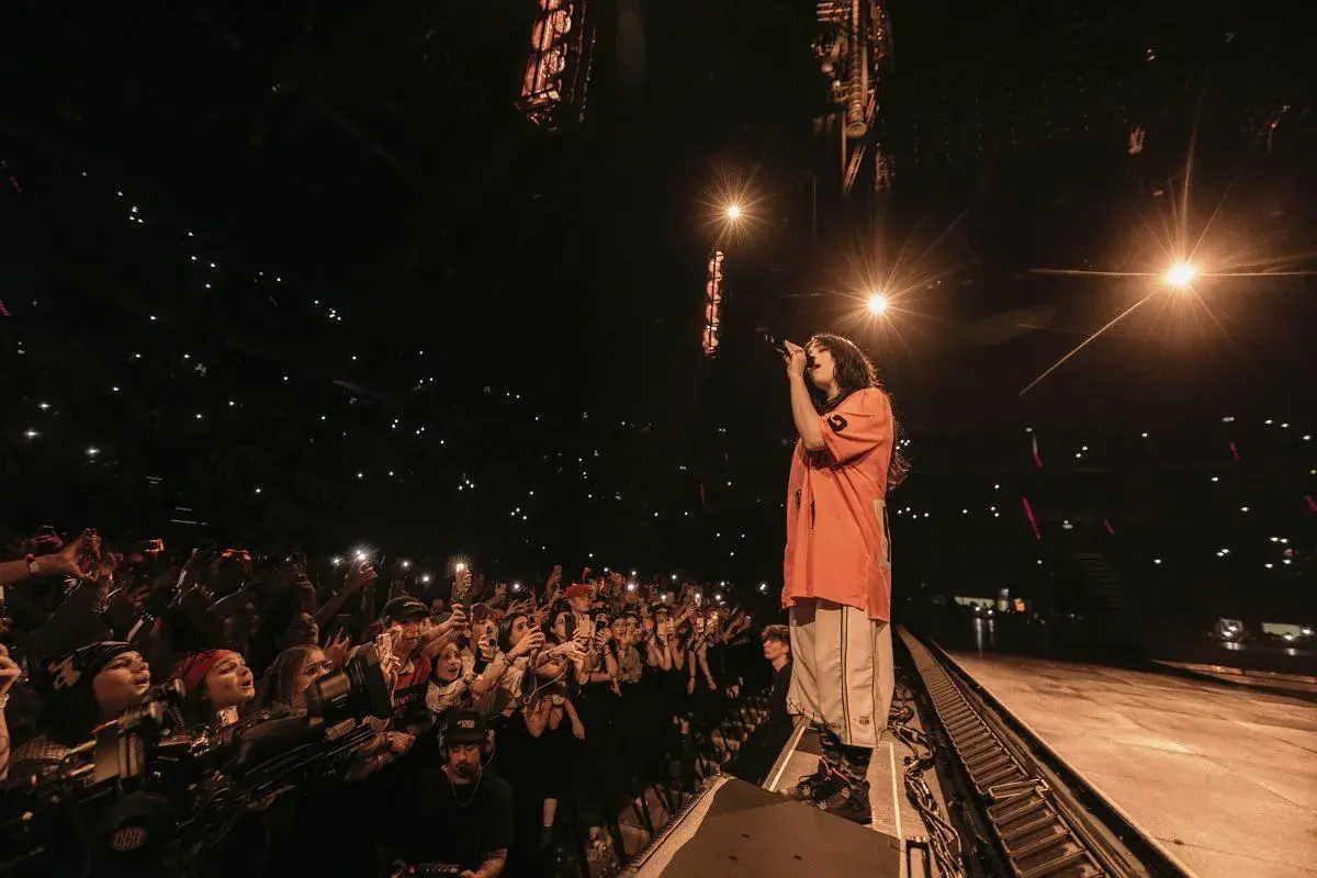 Billie Eilish w Polsce śpiewa dla tłumu fanów, którzy oświetlają scenę telefonami.
