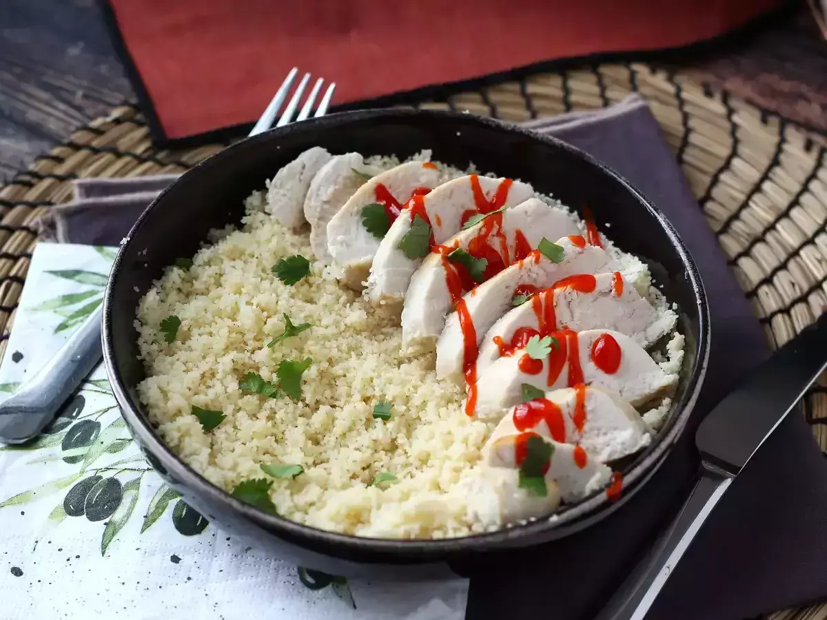 Delizioso pollo in padella a fette, servito su un letto di couscous e guarnito con prezzemolo e salsa piccante.
