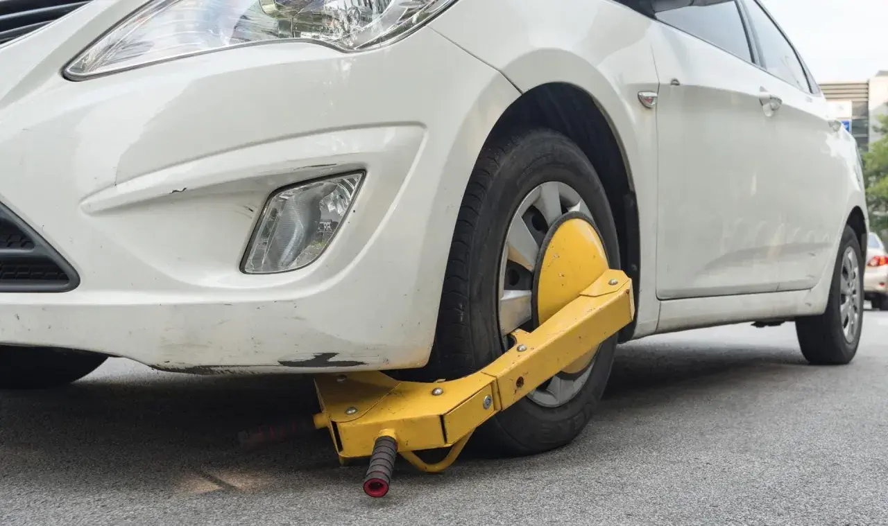 Ruota anteriore di un'auto bianca bloccata da un dispositivo giallo, segno di confisca veicolo.