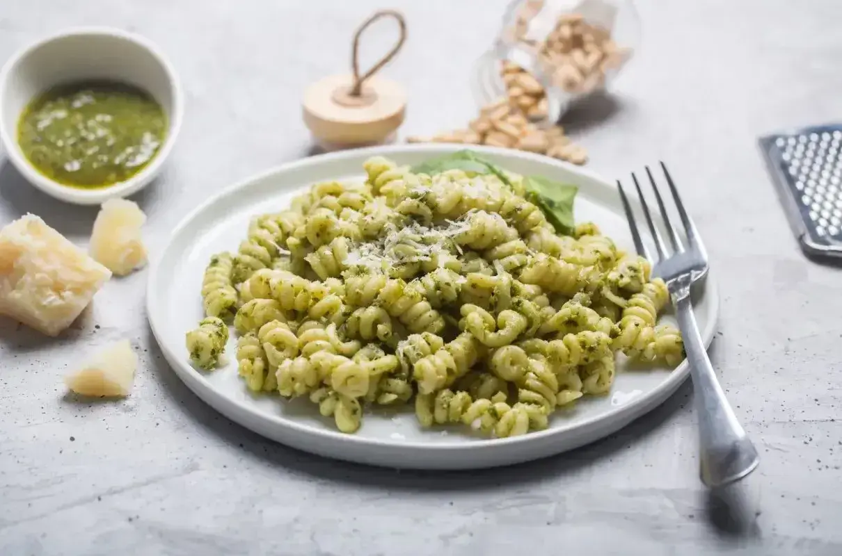 Fusilli z aromatycznym makaronem z pesto ze słoika, posypane parmezanem. Obok miseczka z sosem, kawałki sera i orzeszki piniowe.