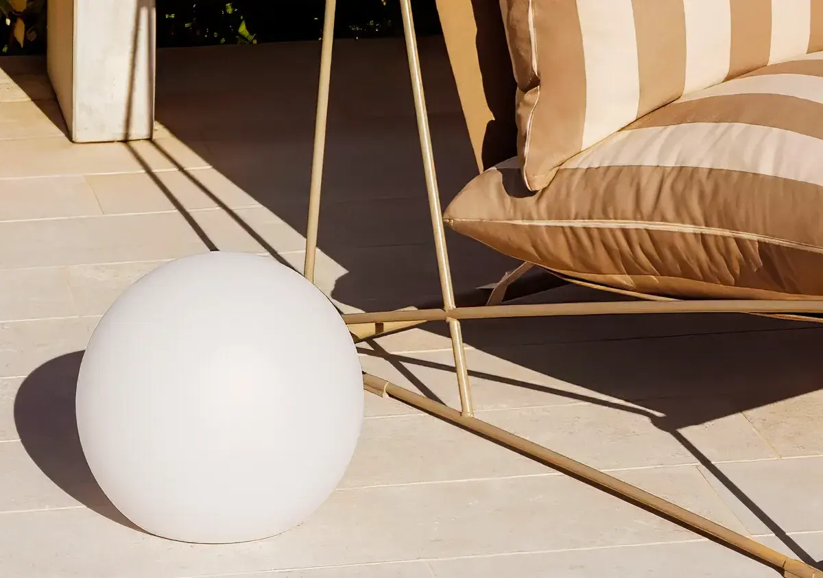 Una lámpara suelo esférica ilumina la terraza junto a un sillón a rayas.