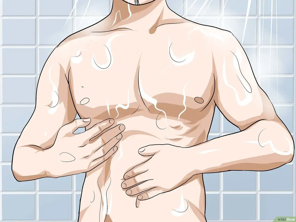 Hombre en la ducha, con agua cayendo sobre su torso. Se toca el pecho, preparándose para depilarse el pecho.