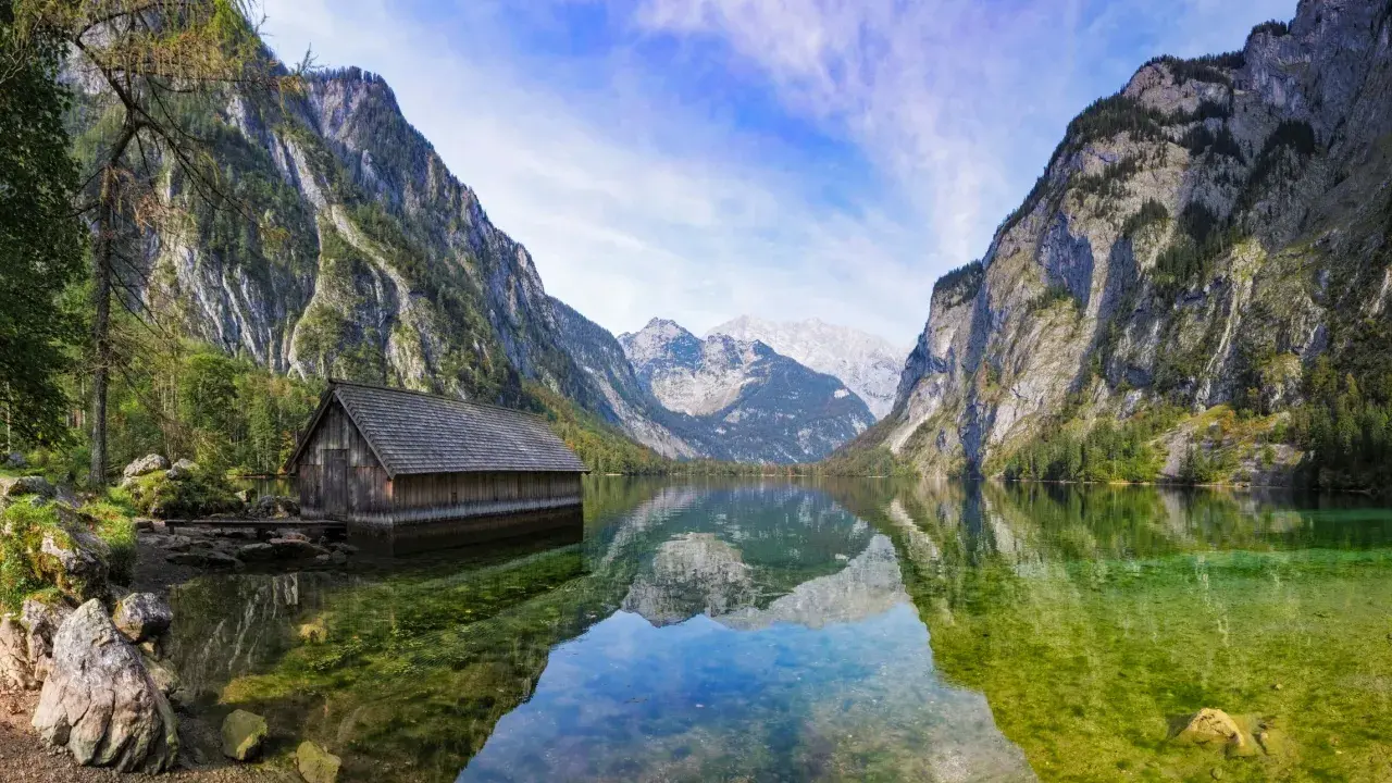 Holzhütte am Königssee, ein Juwel in Bayern, spiegelt sich im klaren Wasser vor majestätischen Bergen.