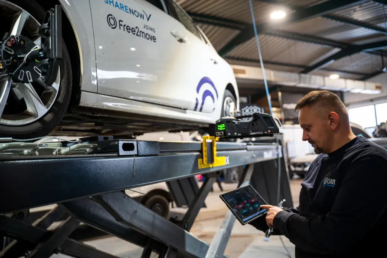 Mechaniker prüft mit Tablet die Achsvermessung an einem Auto. Die Spur verstellt, wird hier präzise eingestellt.
