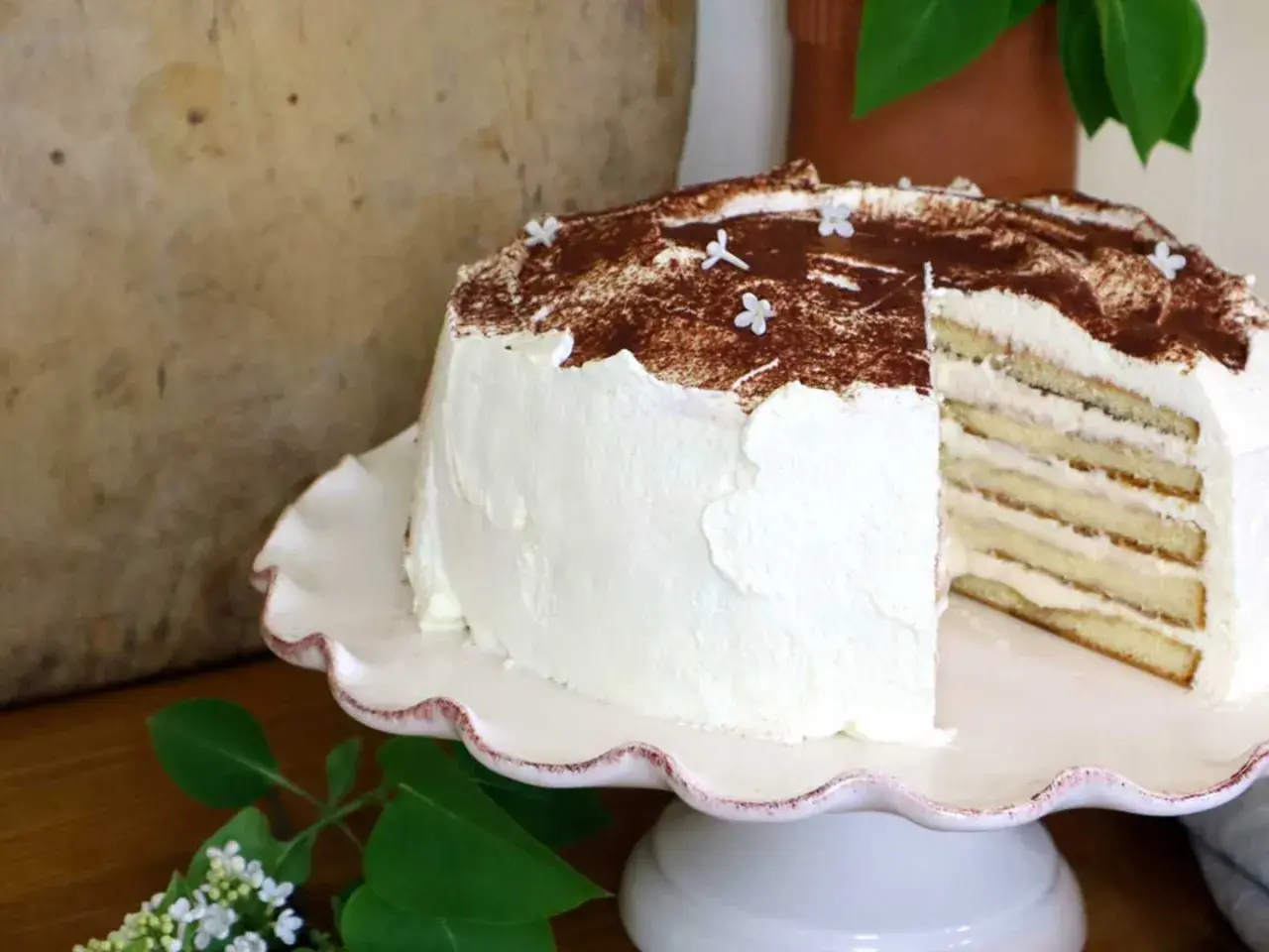 En vacker tiramisu tårta med lager av kräm och kex, toppad med kakao och små vita blommor.