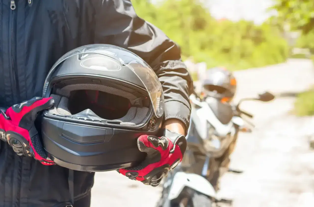 Motocyklista w czerwono-czarnych rękawicach trzyma kask. Warto wiedzieć, co to jest pinlock w kasku, by uniknąć parowania wizjera podczas jazdy.