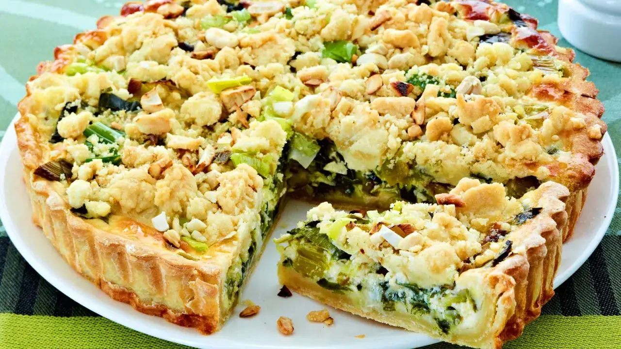 Ein herzhafter Kuchen mit Lauch und einer knusprigen Streuselhaube, auf einem weißen Teller serviert.