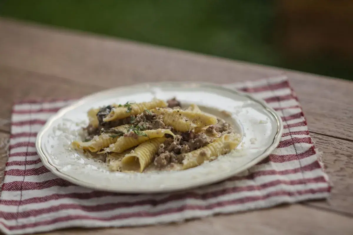 Pasta con ragú bianco, un plato reconfortante con carne picada y hierbas frescas, servido en un plato blanco sobre una servilleta a rayas.